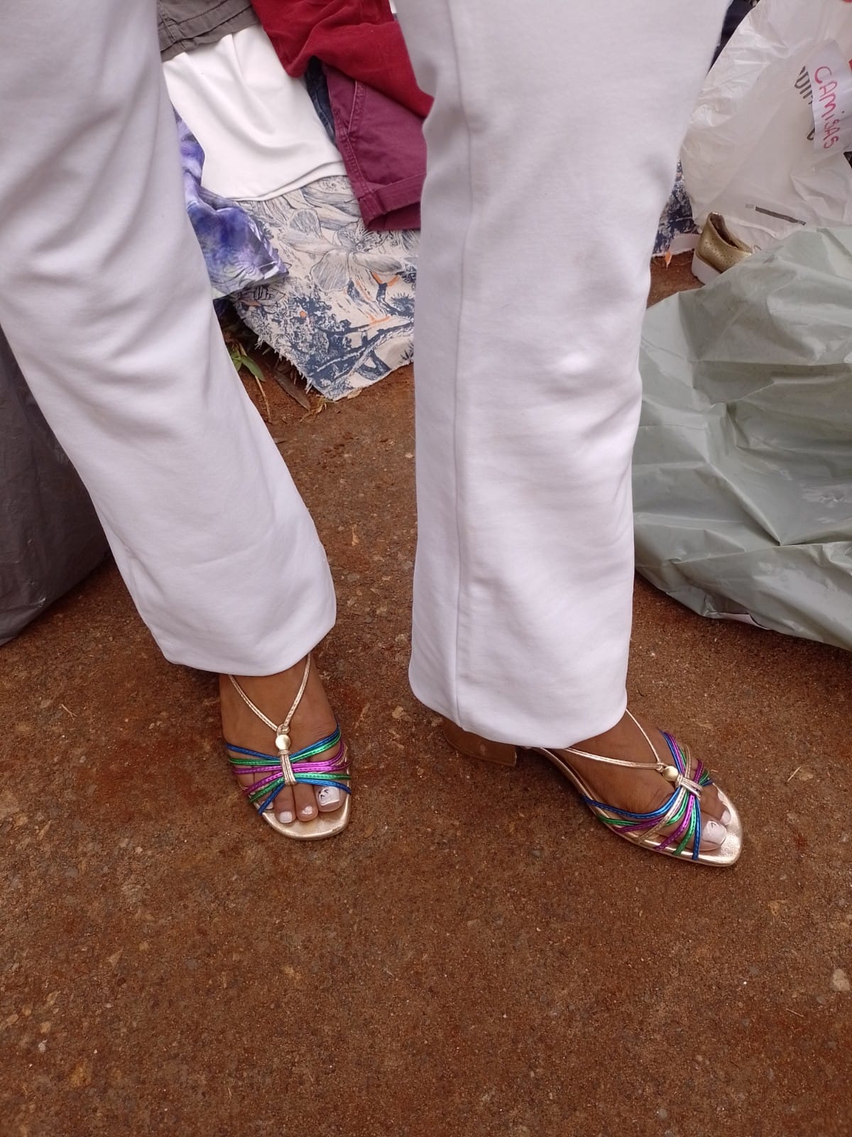 Pernas com calça branca e uma sandália colorida